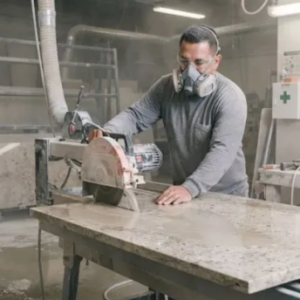 Trabajador fabricando encimeras de piedra artificial expuesto a partículas respirables de sílice durante operaciones de corte y pulido en California.