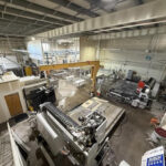 High-angle view of a large industrial workshop with heavy-duty CNC machines and a yellow bridge crane used for engineered stone safety operations.