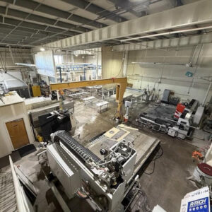 A large industrial workshop with various machinery, worktables, and an overhead crane, viewed from above—its well-lit space hints at the Bloomberg-reported silicosis crisis linked to artificial stone fabrication.