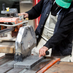 A construction worker uses a wet tile saw to cut an artificial stone countertop.