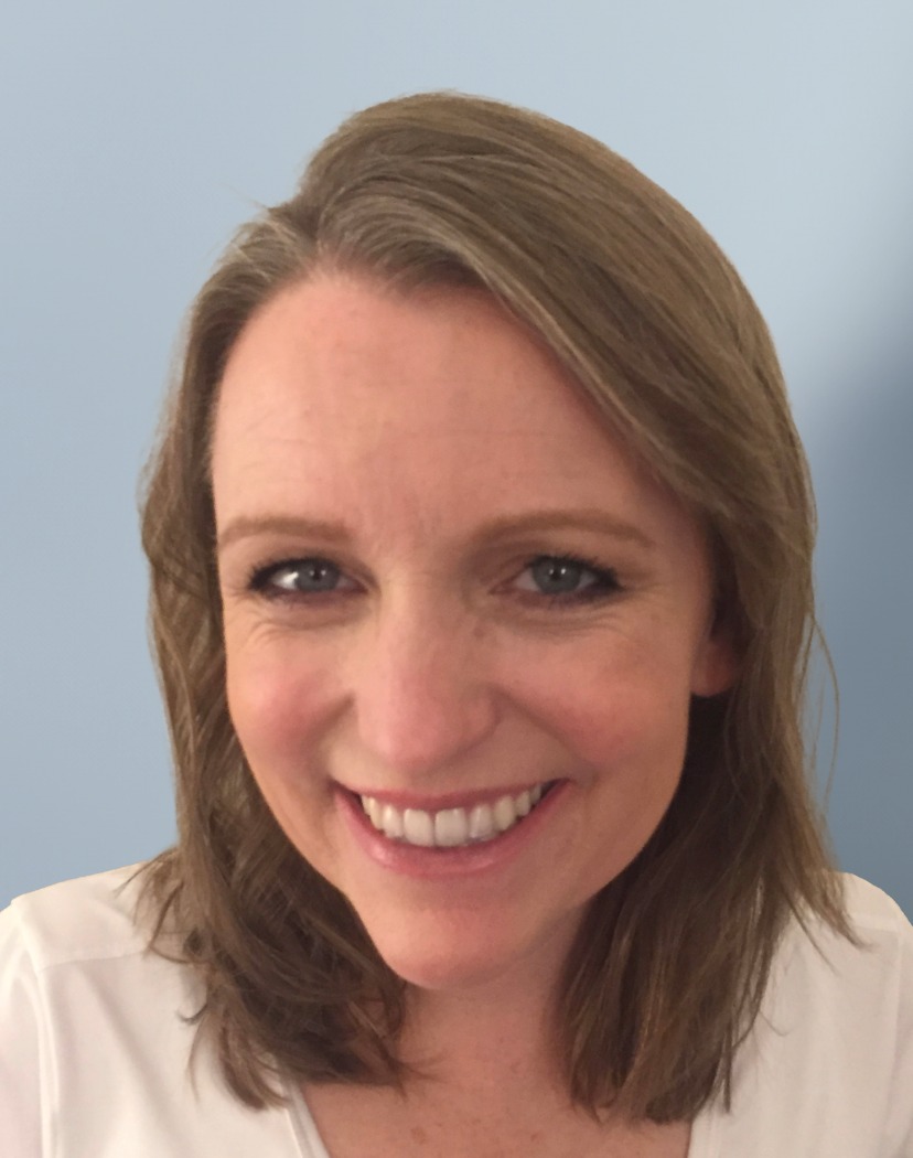 A smiling woman with shoulder-length brown hair wearing a white shirt.
